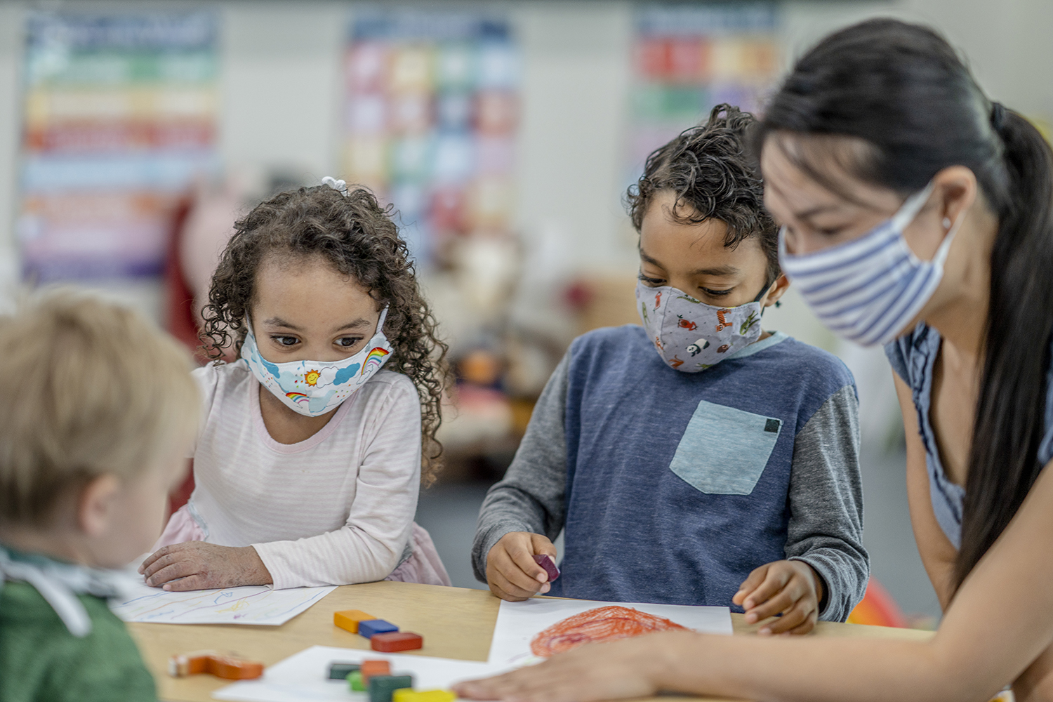 Multi-ethnic group of children coloring at a table while wearing protective face masks to avoid the transfer of germs.