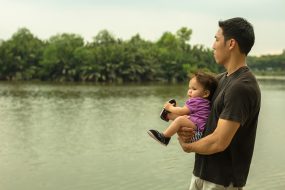 Asian father is taking his child for a walk along the lake carrying the child in his arms