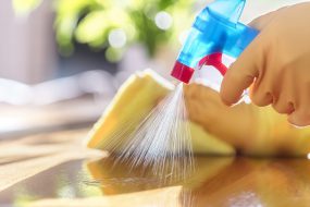 Gloved hand pulls back nozzle on spray cleaner while other gloved hand holds yellow sponge.