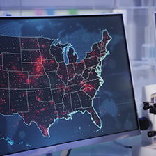 A computer monitor with the united states depicted and various hot-spots of infection illuminated on the map in red.