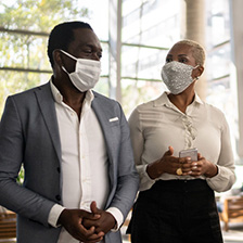 Two people in masks and business clothes talking.