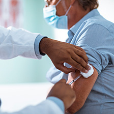 A man with a mask on receiving a shot in the left arm by a medical professional.