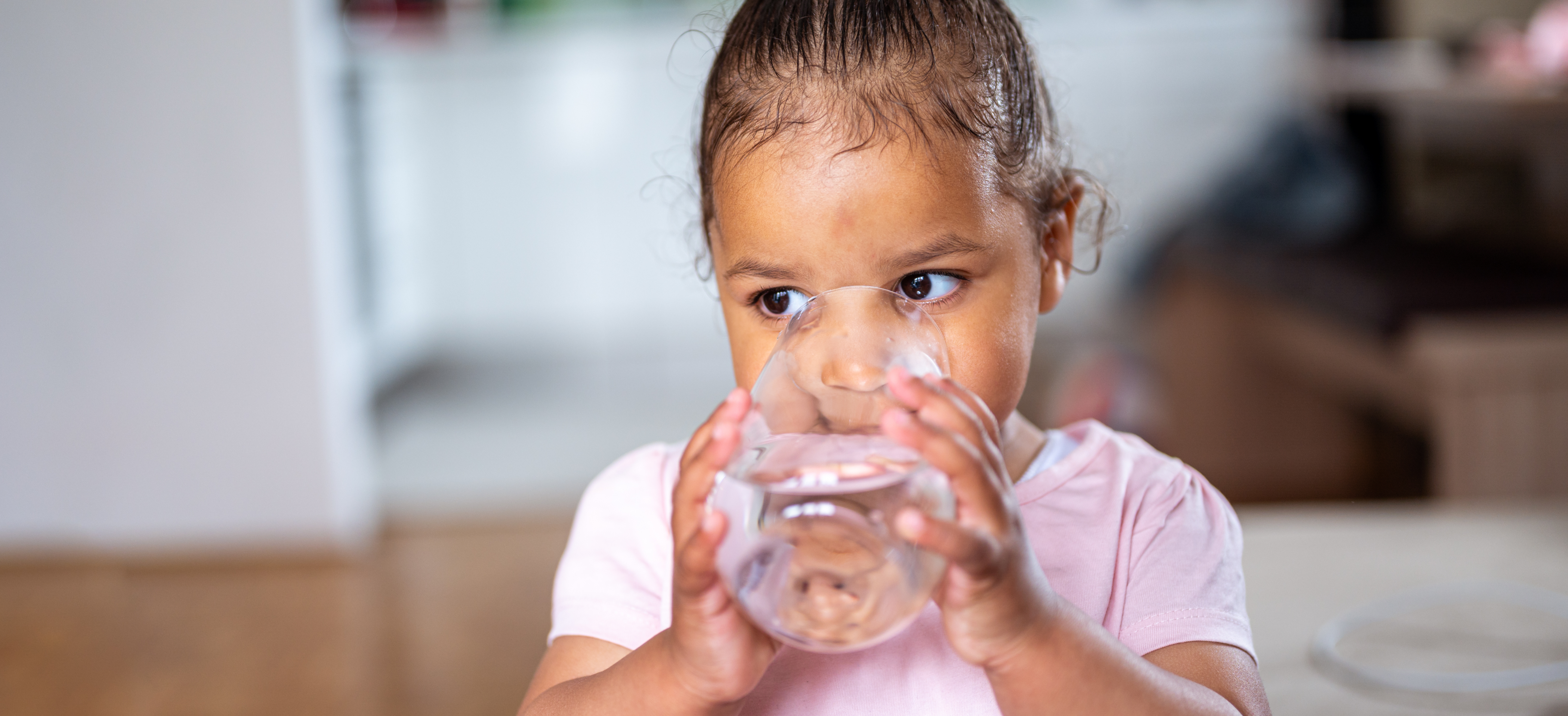 A small child with a pink shirt drinking water out of a glass.