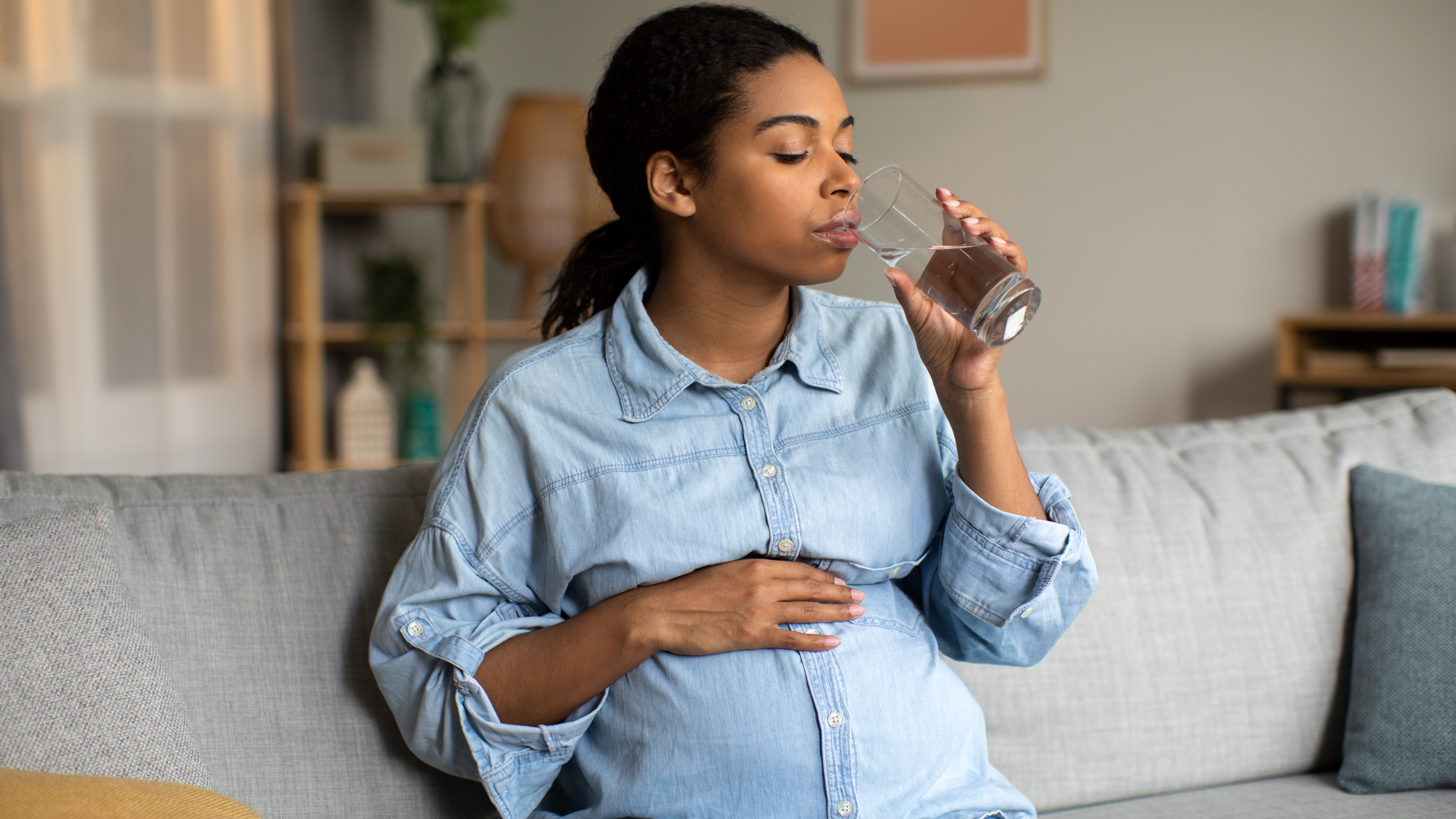 Pregnant African American lady drinking glass of water at home