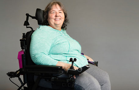 Paciente con esclerosis lateral amiotrófica (ELA) en silla de ruedas sonriendo.