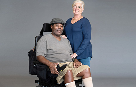 Paciente con esclerosis lateral amiotrófica (ELA) en silla de ruedas sonriendo con un cuidador. Paciente con esclerosis lateral amiotrófica (ELA) en silla de ruedas sonriendo con un cuidador.