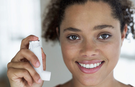 A smiling young women holds an inhaler up to her face.
