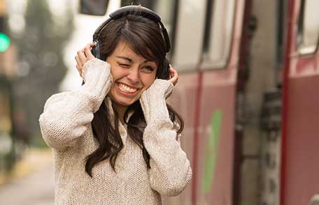 A young woman wearing headphones grimaces when the volume of her music hurts her ears.