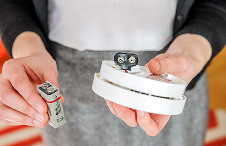 A person replacing a battery in a carbon monoxide detector