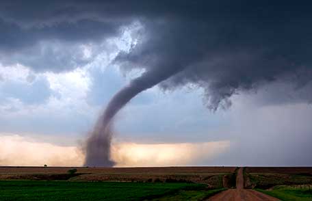 The funnel of a tornado touches the ground in a rural field churning up debris.