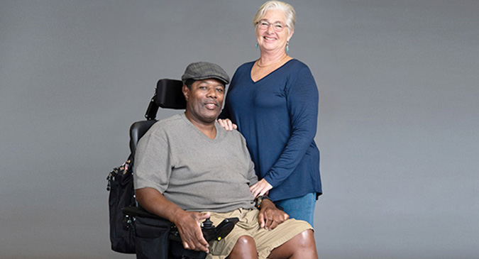 Amyotrophic lateral sclerosis (ALS) patient in a wheelchair smiling with a caregiver.