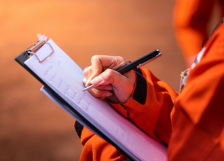 A person wearing orange is writing on a clipboard.