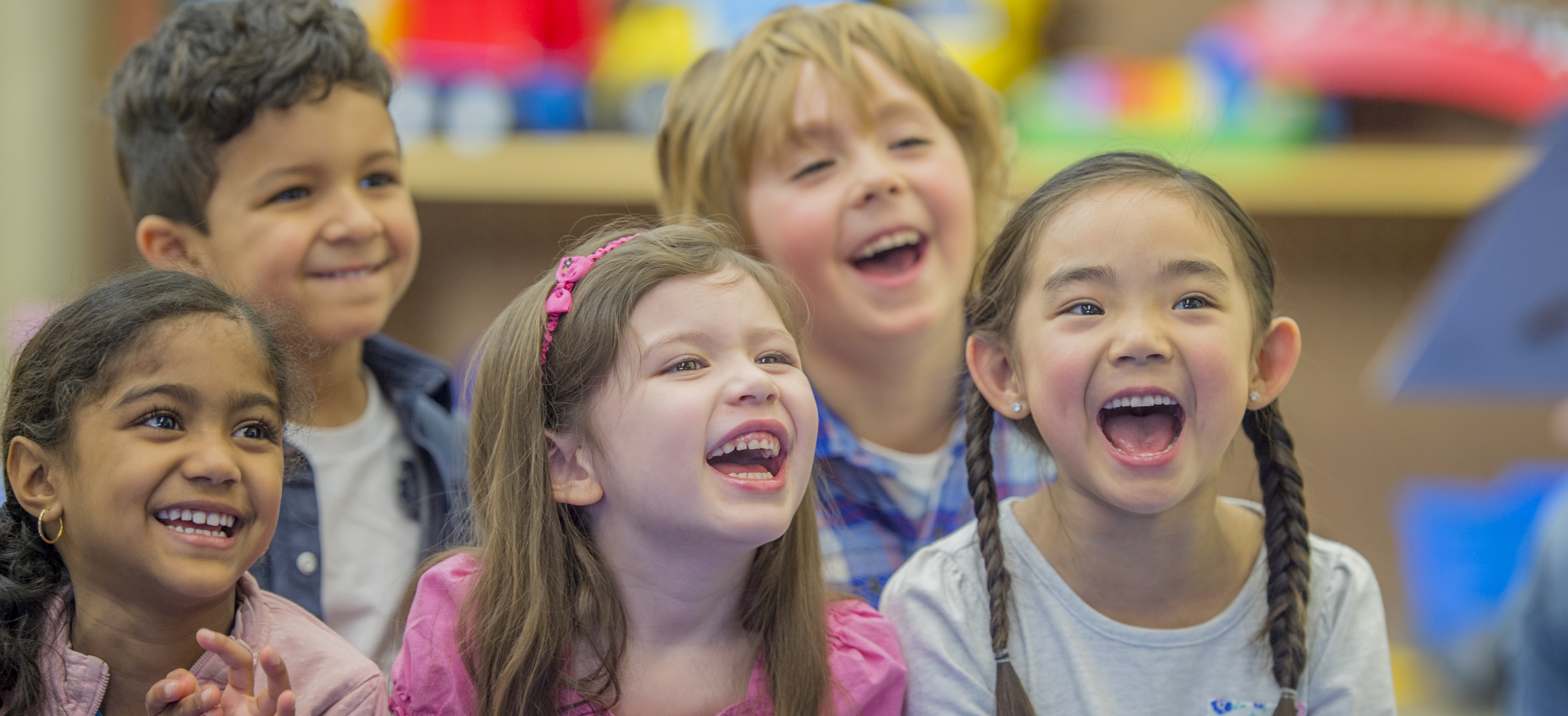 A group of five children laughing with brightly colored toys behind them.