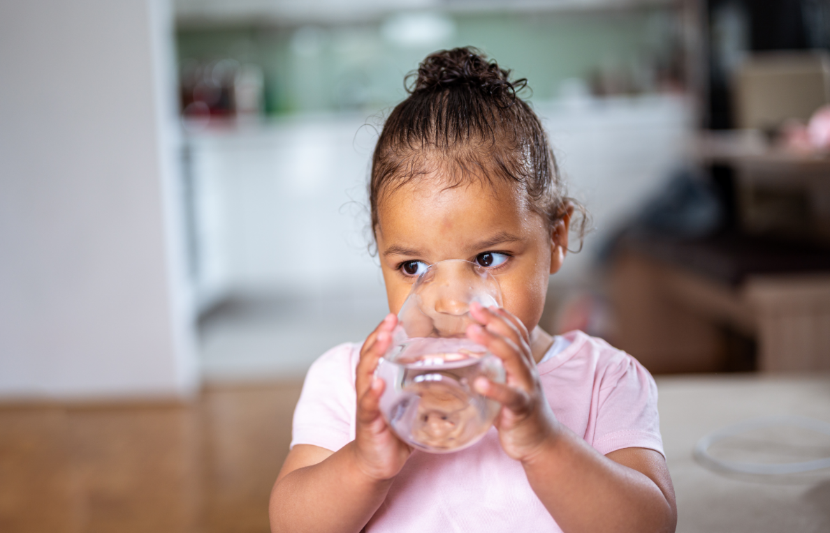 A little girl in a pink shirt drinking a glass of water.