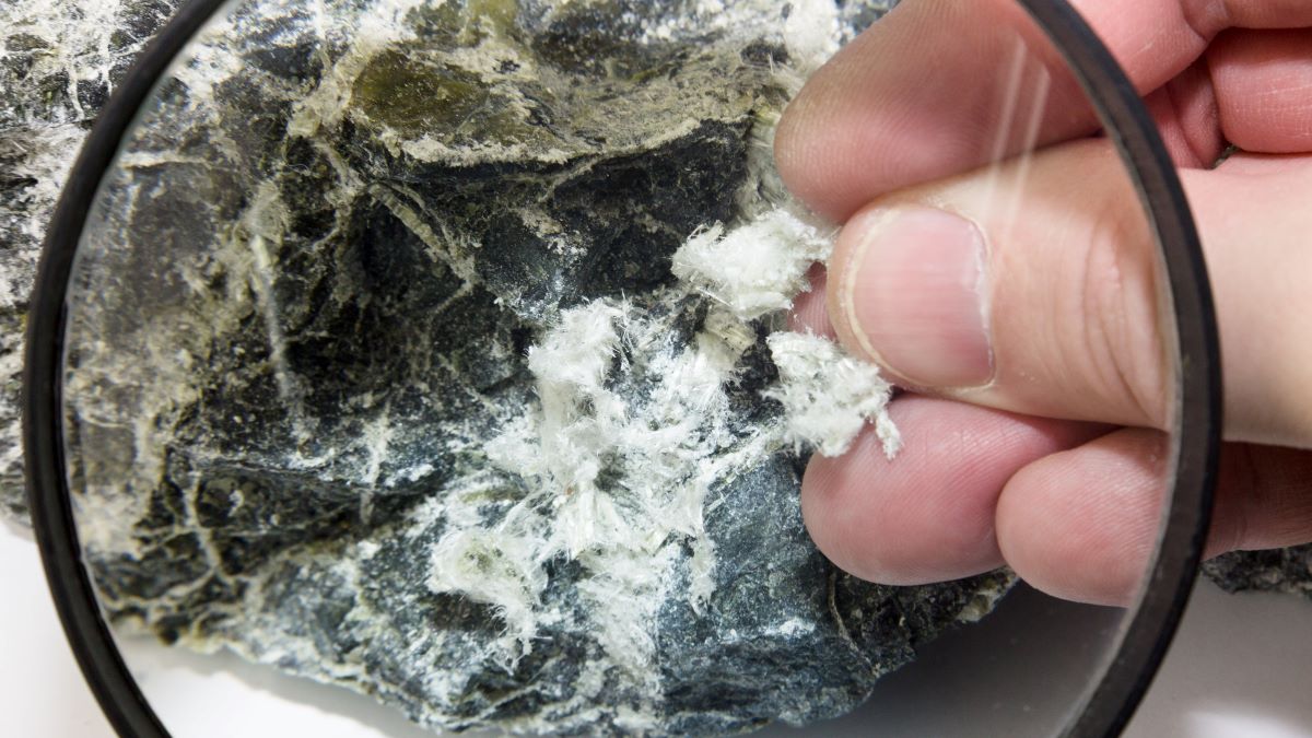 Hand with magnifying glass examines asbestos fibers in stone