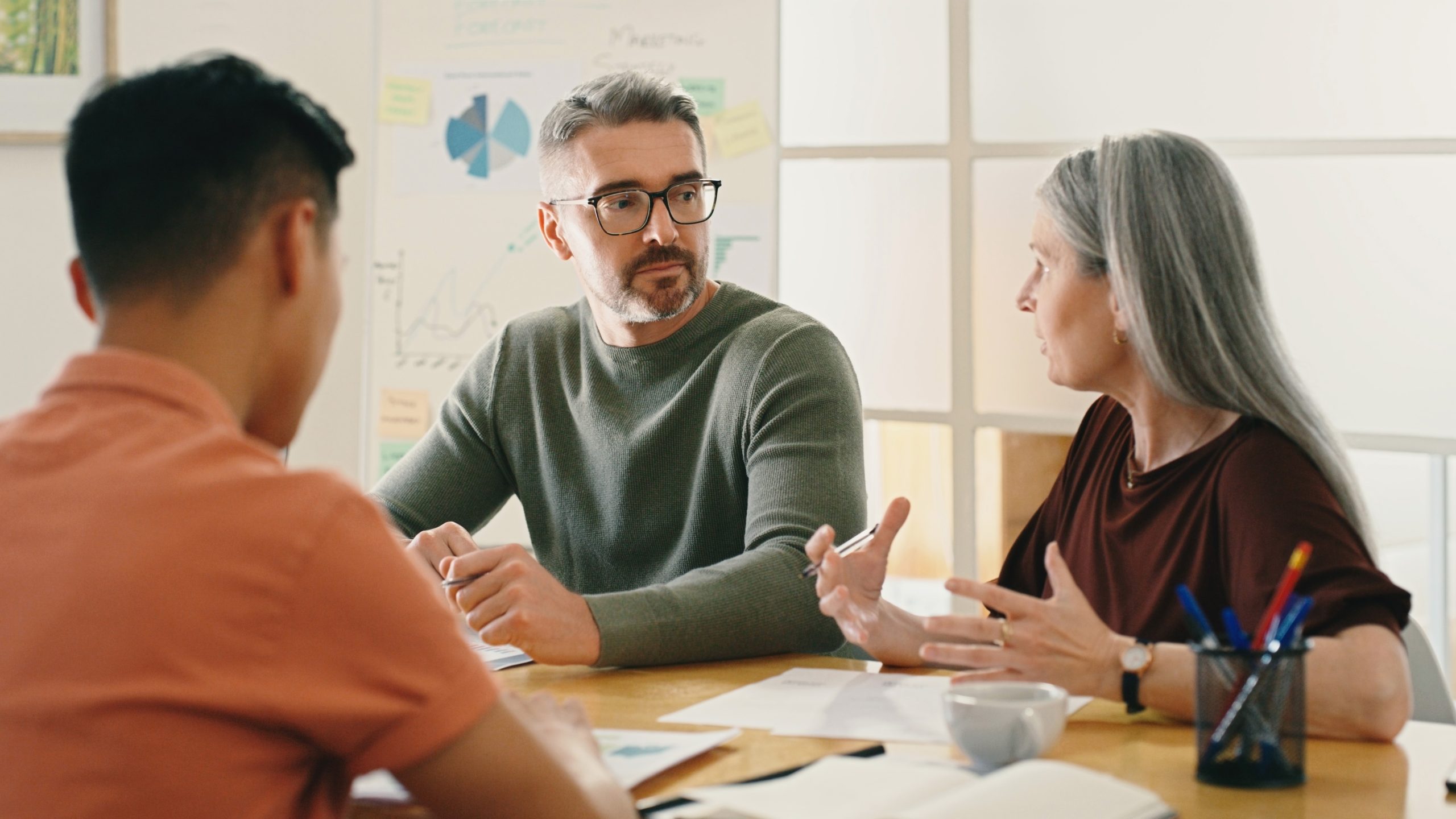 Serious woman in meeting planning, speaking and brainstorming with two male co-workers