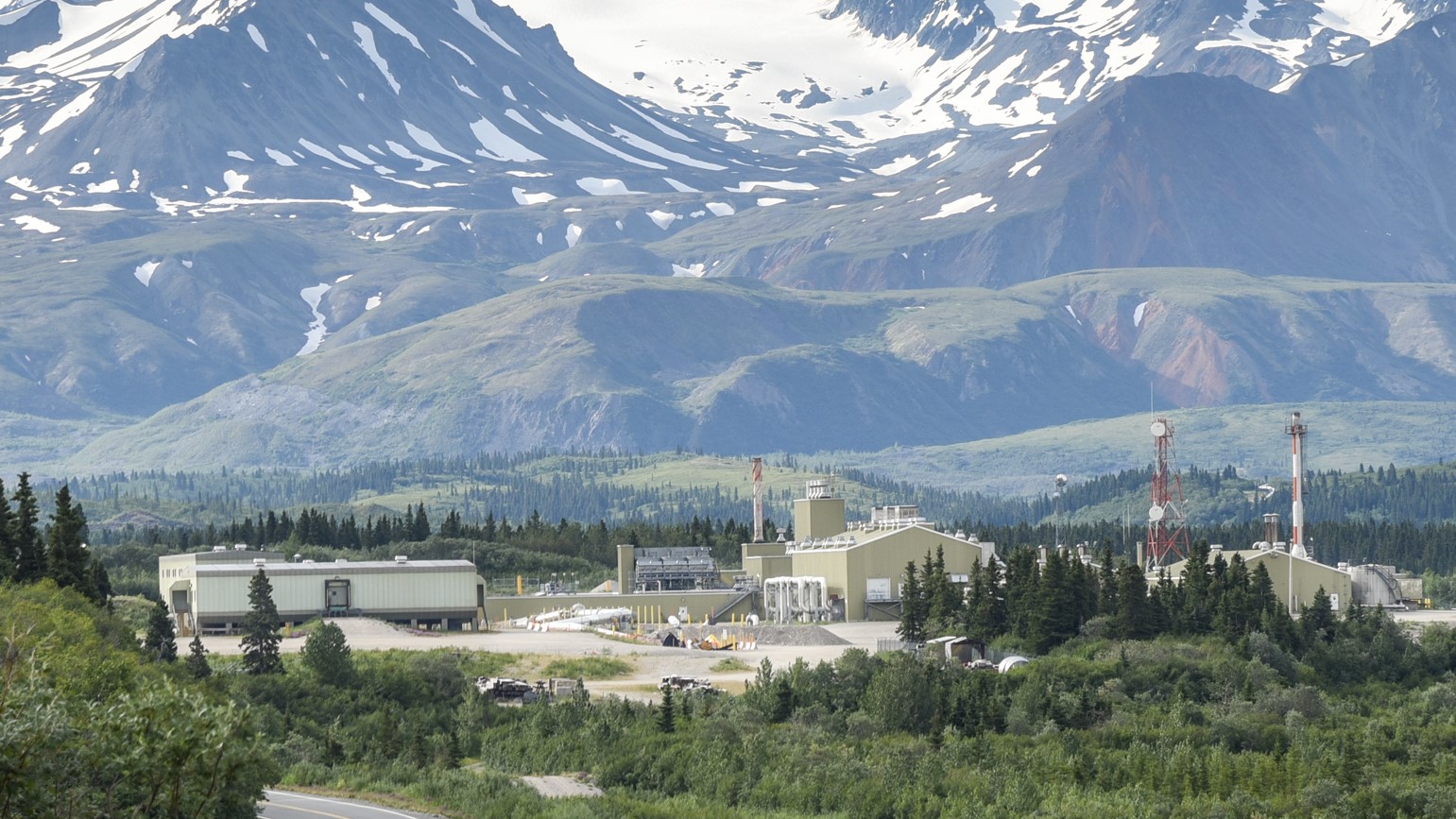 Trans Alaska pipeline pump station in a summer valley with snow-capped mountains.