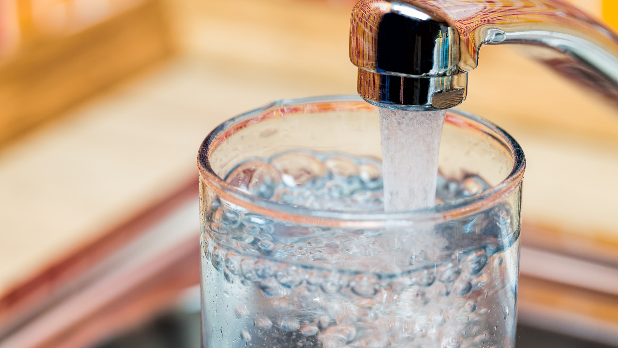 A glass being filled with drinking water from a kitchen faucet.