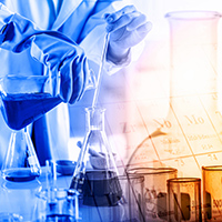 Scientist wearing lab coat and gloves pouring a dark blue chemical from one beaker into another. Other beakers sitting on the table containing chemicals, including amber colored beakers.