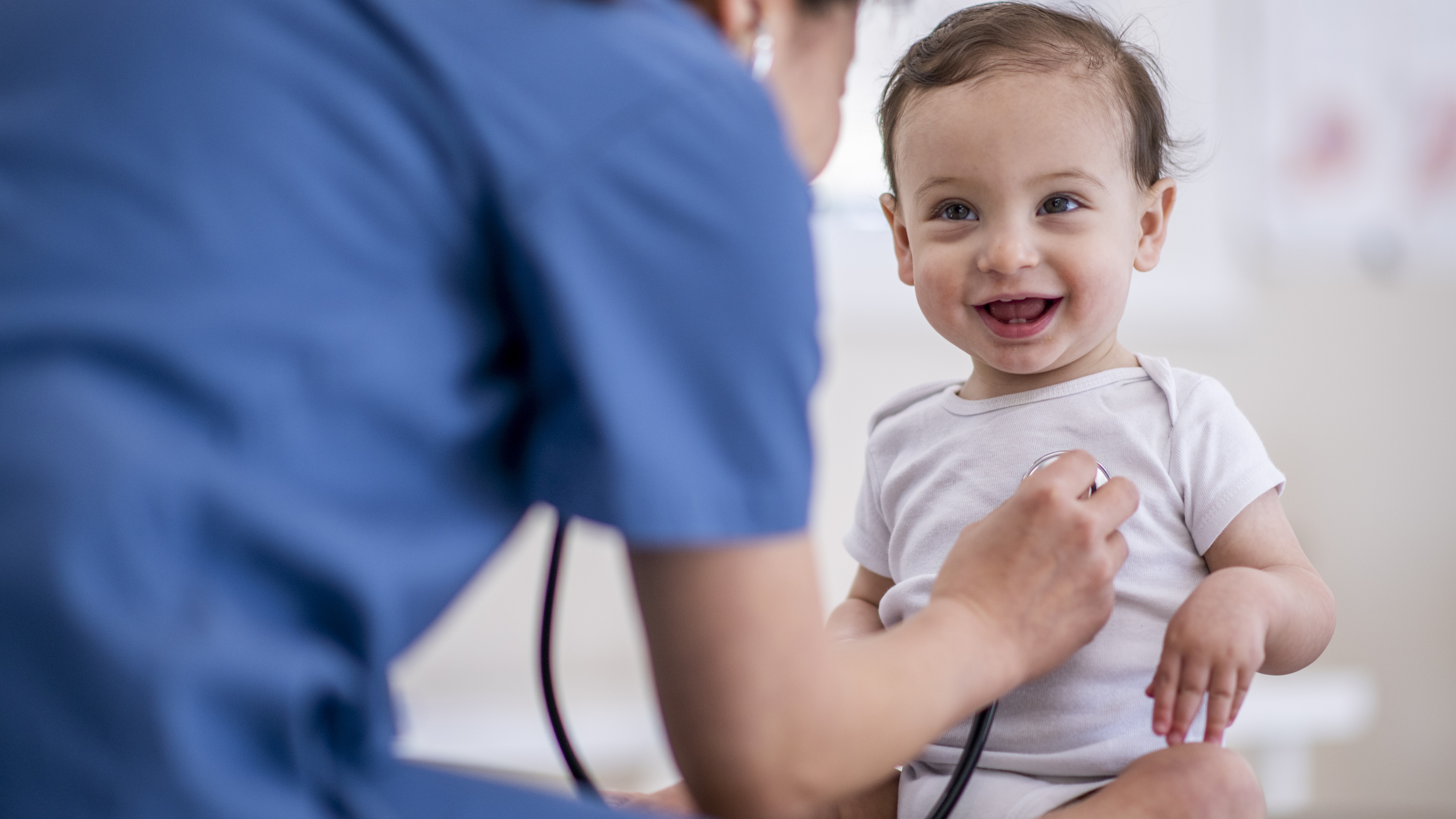 A doctor uses a stethoscope to listen to a smiling toddler's heartbeat.