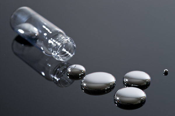 Mercury spilled out of a glass vial gathered in three small puddles of mercury on a mirrored surface.