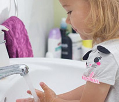 Little girl washing hands in porcelain sink.