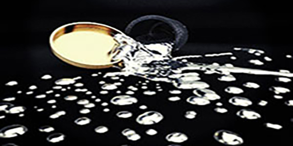 A spilled silvery liquid drops out toward the viewer from a grey container, on a black background