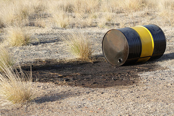 Yellow and black oil drum spilling liquid into a desert landscape
