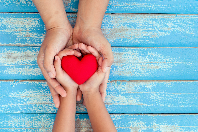 Image of adult and child hands holding a red heart.