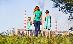 A woman and two girls are holding hands and looking from the distance at an industrial landscape.