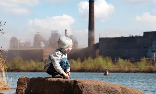 A young boy is looking from the distance at an industrial landscape.